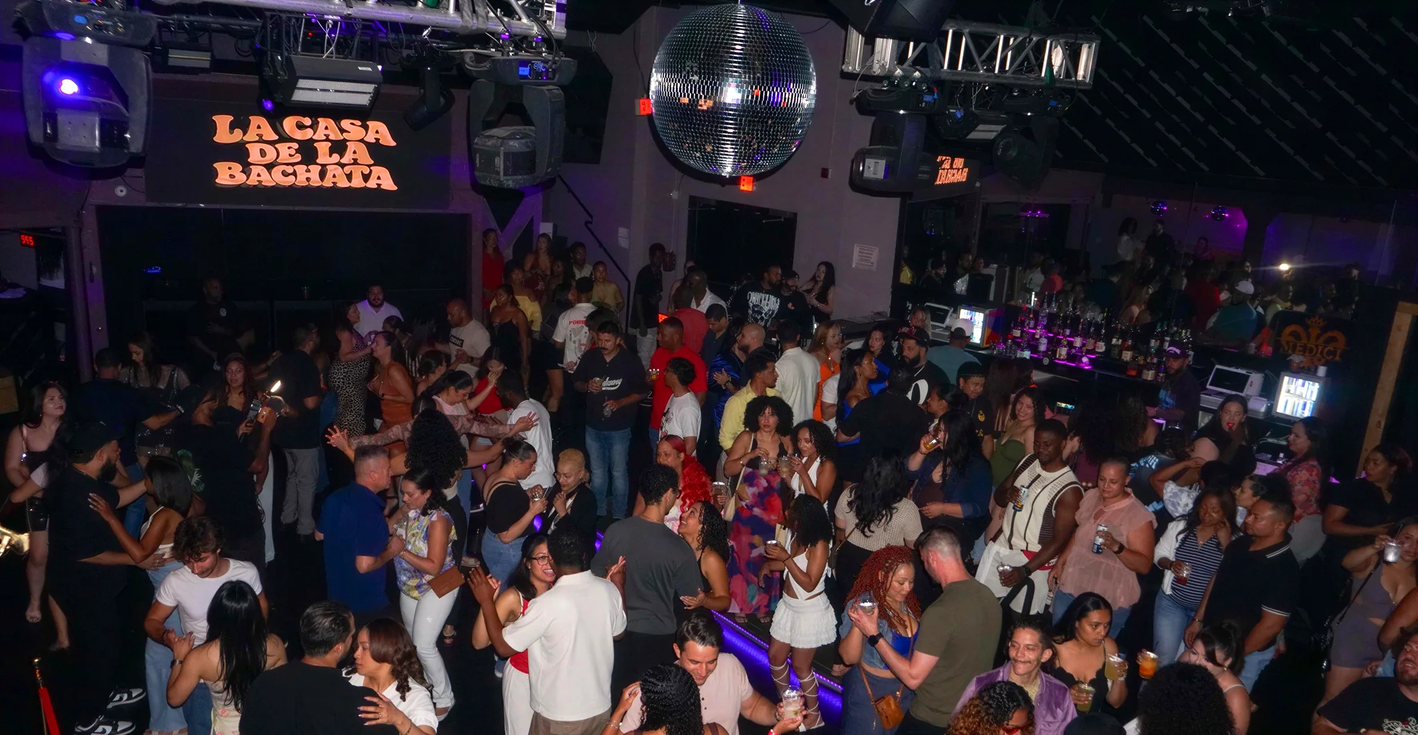 The packed dance floor at La Casa de la Bachata's Tampa night, under a disco ball, with the wordmark lit on the wall